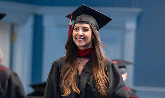 picture of a woman smiling while wearing her graduation cap and gown